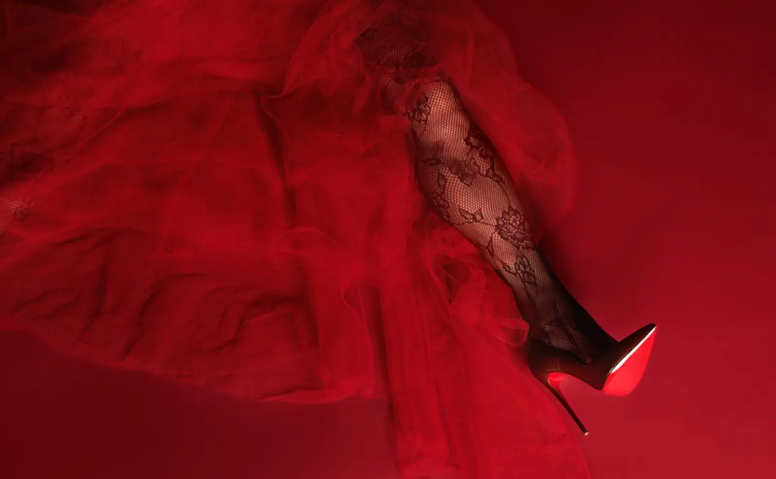 Detail of red tulle and a lace-stockinged leg in a red stiletto