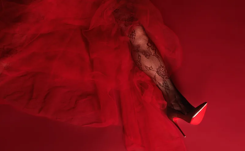 Detail of red tulle and a lace-stockinged leg in a red stiletto