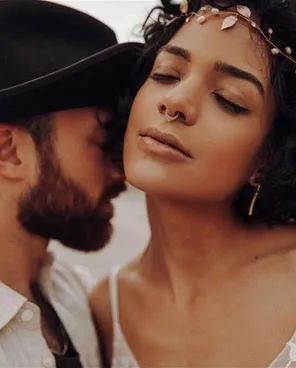 Close portrait of a woman with a leaf headpiece and a bearded man in a hat leaning toward her